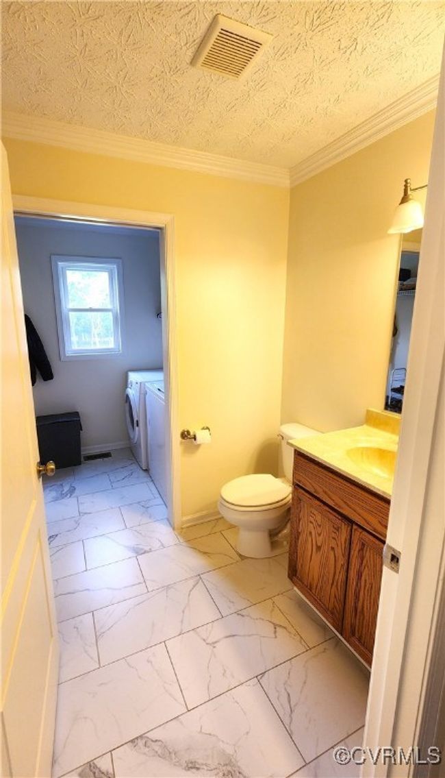 Half bathroom featuring washing machine and dryer, vanity, marble look tile flooring, and ornamental molding | Image 12