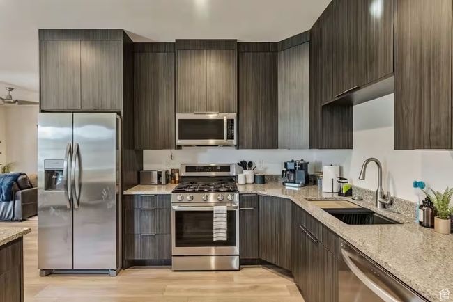 Kitchen featuring light wood-style flooring, stainless steel appliances, a sink, light stone countertops, and modern cabinets | Image 68