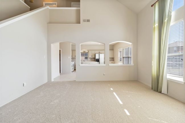 Empty room with visible vents, light carpet, and a towering ceiling | Image 6
