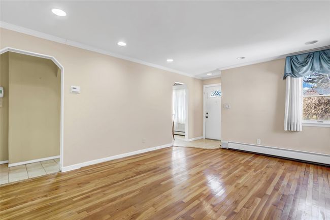 Unfurnished room featuring crown molding, a baseboard heating unit, light wood-type flooring, arched walkways, and a baseboard radiator | Image 6