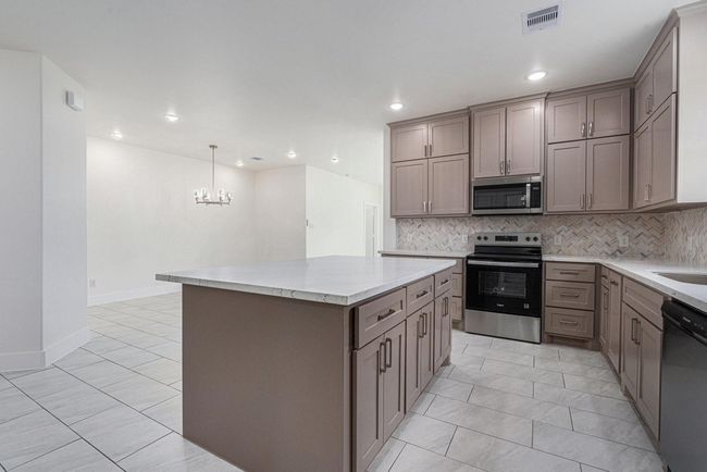 This photo showcases a modern kitchen featuring sleek cabinetry, a large central island with a marble countertop, and stainless steel appliances. The open layout leads into a dining area with tiled flooring and a stylish chandelier, creating a bright and inviting space. | Image 11