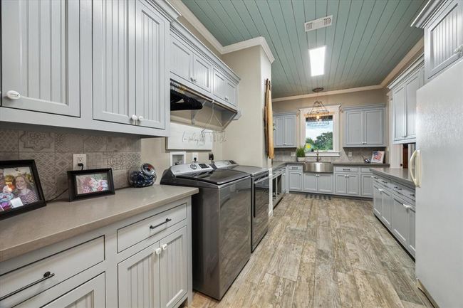 This oversized laundry room is a true standout, featuring a convenient laundry chute from the upstairs bedroom for effortless laundry days. It boasts a stylish lap siding ceiling, elegant quartz countertops, and a spacious sink. Ample storage is provided by custom-built cabinets and a dedicated space for a deep freezer. Thoughtfully designed for pet owners, it includes four custom built-in dog food bowls. Easy-to-maintain ceramic tile flooring and a handy broom closet complete this functional yet beautiful. | Image 24