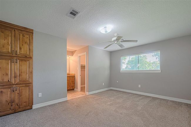 Spacious primary bedroom offers plenty of natural lighting from windows on two walls, a built-in wall storage cabinet, and an en-suite bathroom | Image 12
