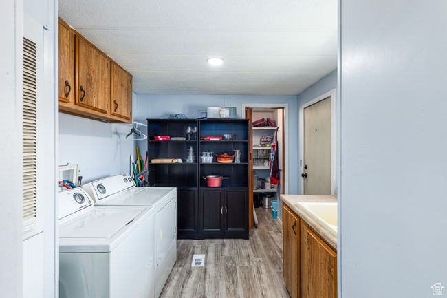 Laundry area featuring light wood finished floors, washing machine and dryer, a sink, and cabinet space | Image 16