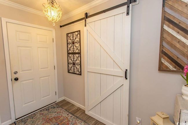 Doorway to Den with wood finished floors, a barn door, ornamental molding, and a chandelier | Image 12