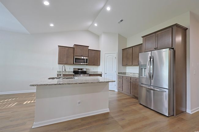 Kitchen with stainless steel appliances, dark brown cabinetry, an island with sink, light stone counters, and light wood-type flooring | Image 5