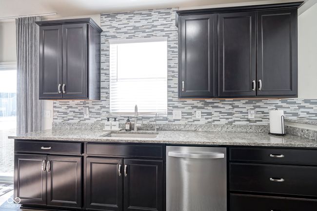 kitchen featuring light stone counters, a sink, dishwasher, decorative backsplash, and dark cabinets | Image 22