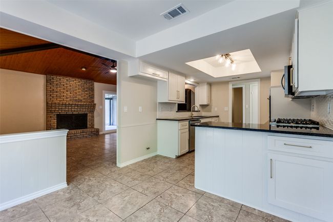 Kitchen featuring light tile patterned floors, a raised ceiling, a brick fireplace, gas stovetop, and tasteful backsplash | Image 11
