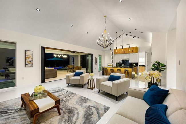 Step into this exquisite open-concept living space, where soaring vaulted ceilings and sleek recessed lighting create an airy, elegant ambiance. The seamless indoor-outdoor flow is highlighted by expansive glass sliders that lead to a covered patio and sparkling pool area. The gourmet kitchen boasts a striking combination of natural wood cabinetry, polished countertops, and modern pendant lighting, making it the perfect centerpiece for stylish entertaining and everyday living. | Image 7