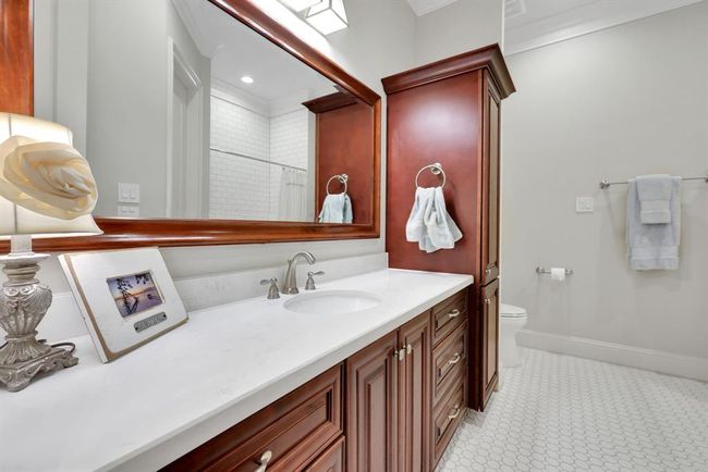 The ensuite bathroom offers high ceilings and a single, oversized vanity topped with elegant quartz countertops and an undermount sink. Brushed chrome plumbing and lighting fixtures lend a modern touch, while the tub/shower combination is set against a backdrop of crisp white tilework. The space is grounded by simple, yet stunning white octagon tile flooring, bringing a clean and timeless finish. | Image 21