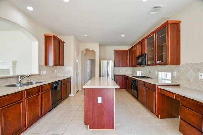 Spacious kitchen featuring a large island, 42" tall cabinets, silestone countertops, gas cooktop and built-in desk station. | Image 13