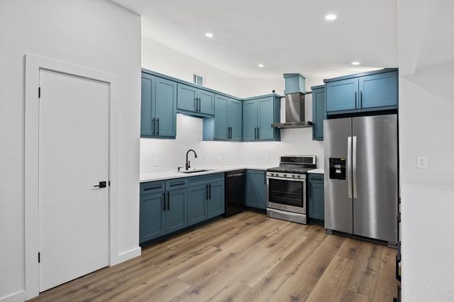 Kitchen with stainless steel appliances, wall chimney range hood, blue cabinets, light wood finished floors, and recessed lighting | Image 8