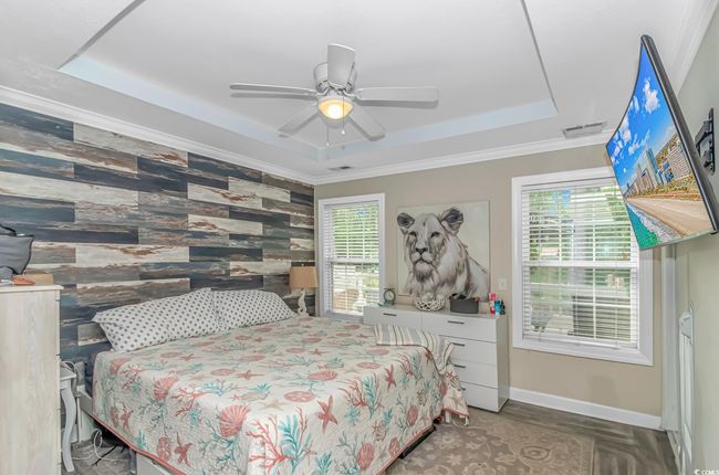 Bedroom featuring a raised ceiling, multiple windows, baseboards, ornamental molding, and wooden walls | Image 16
