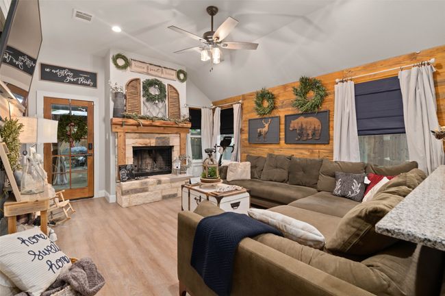Living area featuring ceiling fan, a stone fireplace, wood walls, wood finished floors, and lofted ceiling | Image 10