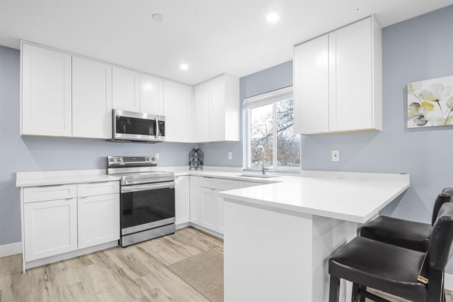 Kitchen featuring white cabinetry, a kitchen bar, stainless steel appliances, a sink, and a peninsula | Image 9
