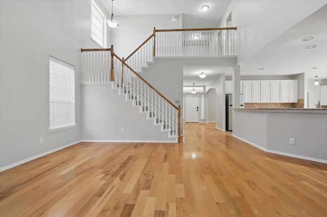 Unfurnished living room with a high ceiling, light wood finished floors, stairway, and baseboards | Image 10