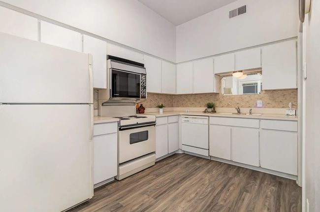 Kitchen featuring white appliances, light countertops, dark wood-style flooring, white cabinets, and a sink | Image 5