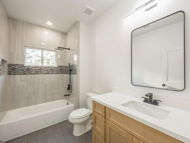 The guest bath features a combination tub/shower with stunning vertical tile surround and mosaic accent, quartz countertop, and modern matte black hardware. | Image 33