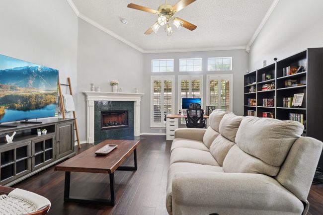 Living area with crown molding, a ceiling fan, a textured ceiling, a fireplace, and wood finished floors | Image 4