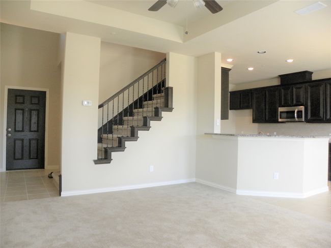 Unfurnished living room featuring a ceiling fan, light colored carpet, recessed lighting, light tile patterned floors, and stairs | Image 5