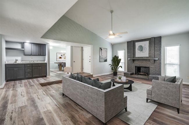 Living area featuring wood finished floors, a ceiling fan, high vaulted ceiling, a fireplace, and baseboards | Image 5