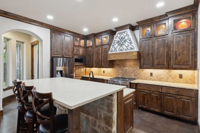 Kitchen featuring black stainless steel appliances, Jenn-Air professional gas oven & cooktop, arched walkways, decorative backsplash, Quartz & Granite countertops, and premium range hood, LED dimmable lighting in ceiling and LED under-cabinet lights | Image 8