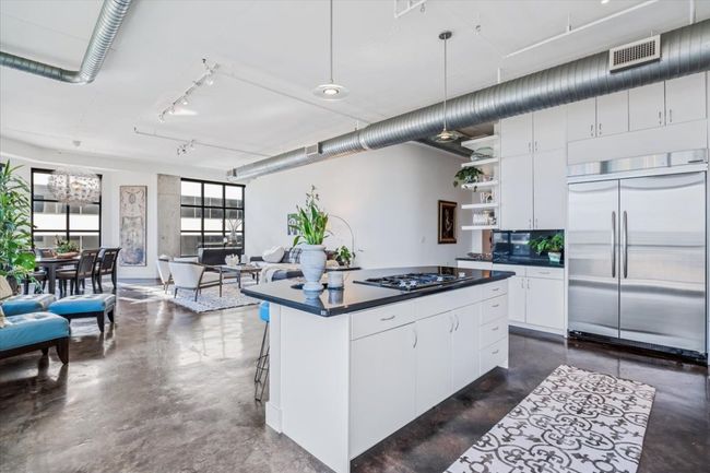 Kitchen featuring finished concrete floors, dark countertops, stainless steel built in refrigerator, track lighting, and open shelves | Image 6