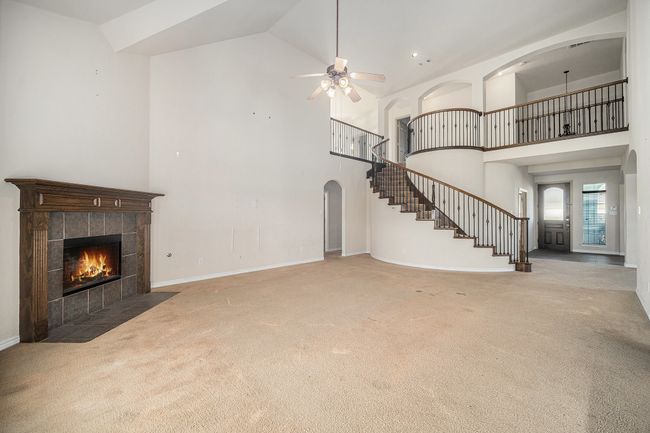 Unfurnished living room featuring high vaulted ceiling, carpet flooring, stairway, a tiled fireplace, and a ceiling fan | Image 7