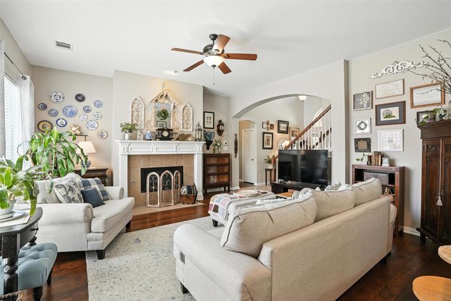 Living area featuring arched walkways, a ceiling fan, dark wood finished floors, stairway, and a tile fireplace | Image 7