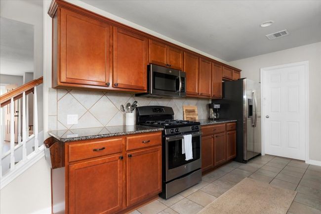 Kitchen with stainless steel appliances, backsplash, dark stone counters, and brown cabinets | Image 8