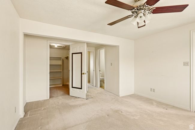 Unfurnished bedroom with light colored carpet, a walk in closet, a closet, a ceiling fan, and ensuite bath | Image 19