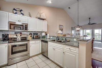 Kitchen featuring kitchen peninsula, stainless steel appliances, white cabinets, and hanging light fixtures | Image 3