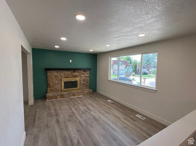 Unfurnished living room featuring recessed lighting, wood finished floors, a textured ceiling, a stone fireplace, and an accent wall | Image 7