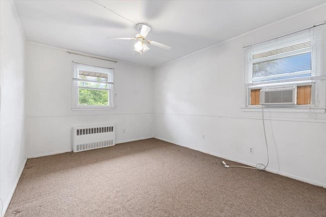 Carpeted spare room featuring radiator, ceiling fan, baseboards, cooling unit, and crown molding | Image 9
