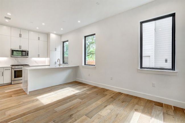 Kitchen featuring appliances with stainless steel finishes, light countertops, white cabinets, a peninsula, and light wood finished floors | Image 11