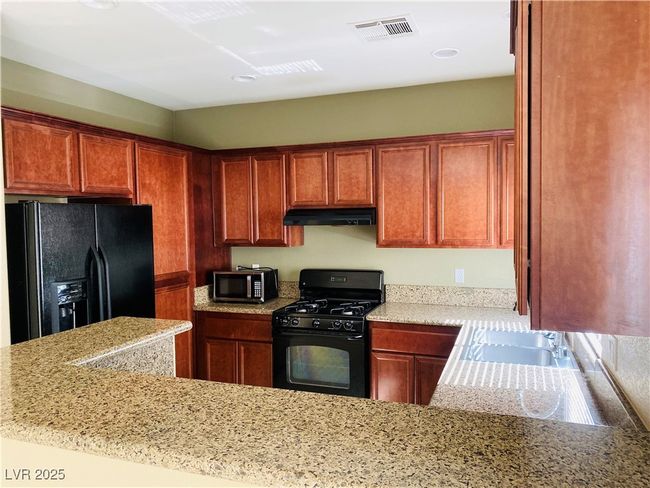 Kitchen with visible vents, brown cabinets, black appliances, under cabinet range hood, and a sink | Image 7