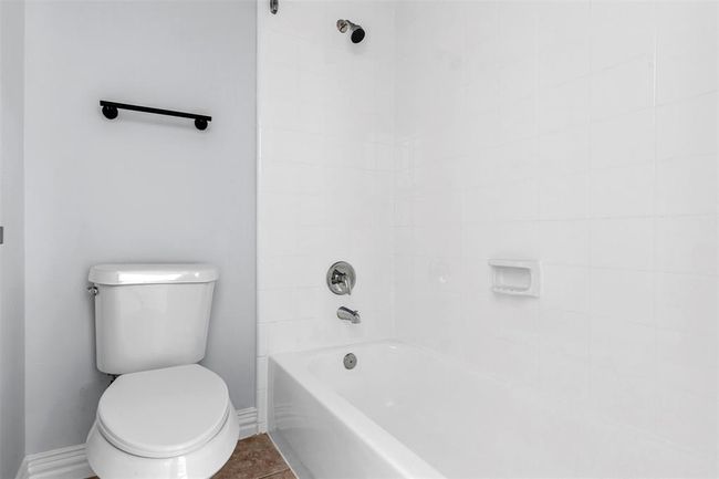 This photo shows a clean, minimal bathroom with a white bathtub and shower combo, a toilet, and light gray walls. It's simple and functional, ideal for a fresh start. | Image 37