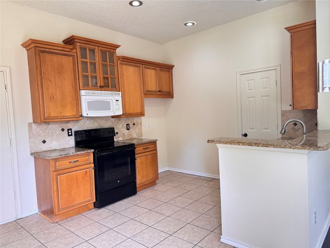 Kitchen featuring white microwave, black range with electric stovetop, brown cabinetry, recessed lighting, and a textured ceiling | Image 6