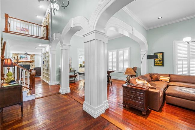Step into elegance with grand columned archways leading to expansive living spaces with high ceilings and abundant natural light. The timeless charm of plantation shutters, intricate crown molding, and original wood floors complement the seamless open floor plan, while vintage lighting fixtures add a touch of classic sophistication. | Image 6