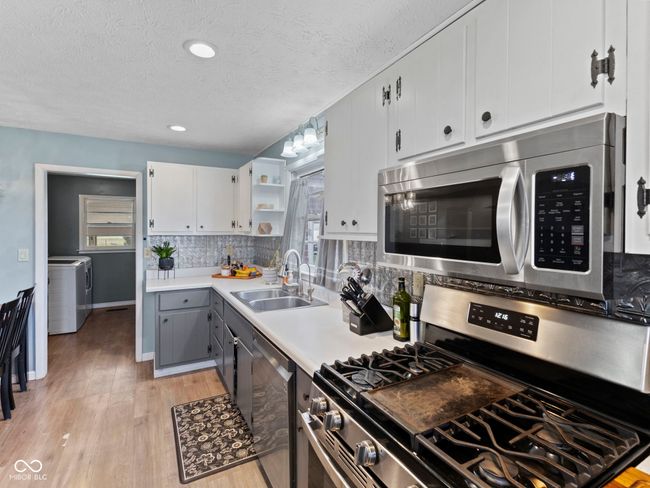 kitchen featuring light wood-type flooring, gray cabinets, stainless steel appliances, a sink, and washer / dryer | Image 10