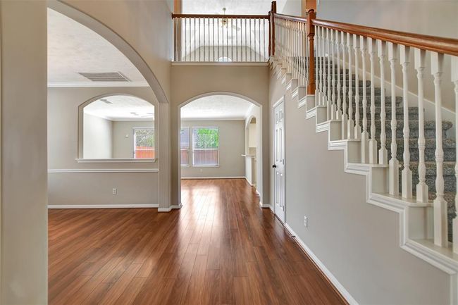 This welcoming home features a spacious entryway with elegant hardwood floors, a grand staircase with white balusters, and large archways leading to bright living areas. | Image 7