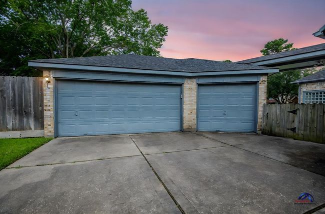 A spacious 3 car garage, set against a backdrop of lush greenery. The driveway is wide, providing ample parking space. | Image 4
