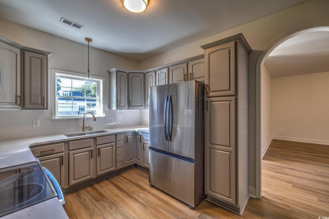Kitchen with freestanding refrigerator, gray cabinetry, wood finished floors, tasteful backsplash, and arched walkways | Image 27