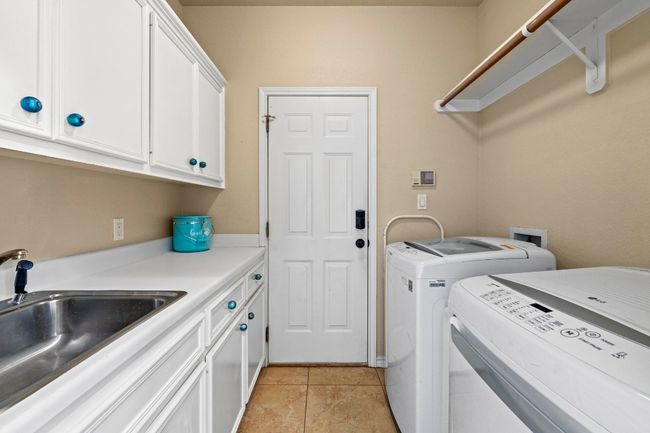 Laundry room featuring a sink, cabinet space, light tile patterned floors, and washing machine and clothes dryer | Image 33