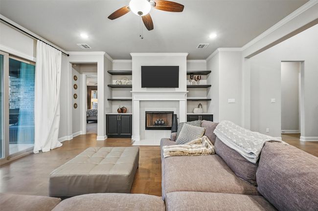 Living room featuring ornamental molding, a ceiling fan, wood finished floors, a fireplace, and built in shelves | Image 13