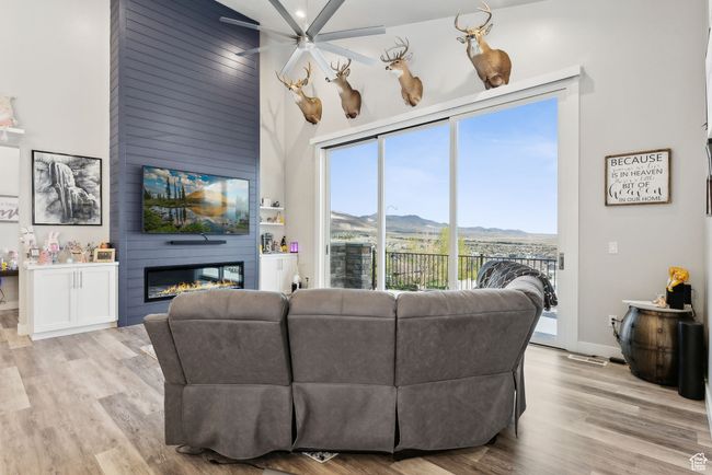 Living room featuring light wood-style floors, ceiling fan, a fireplace, visible vents, and a towering ceiling | Image 53