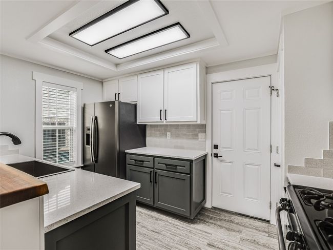 Kitchen with a sink, white cabinetry, stainless steel fridge with ice dispenser, decorative backsplash, and range with gas cooktop | Image 7