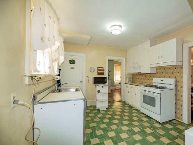 Kitchen with white gas stove, dark floors, white cabinets, black microwave, and light countertops | Image 17