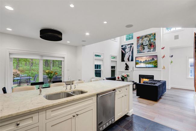 Kitchen featuring stainless steel dishwasher, a sink, light stone countertops, open floor plan, and a glass covered fireplace | Image 10