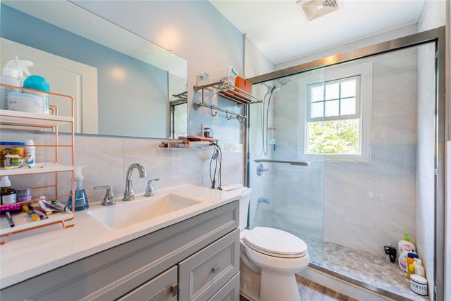 Bathroom with toilet, a tile shower, vanity, and tasteful backsplash | Image 7